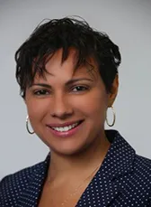 A head shot of a woman wearing a blue dress blouse with white polka dots smiles into the camera